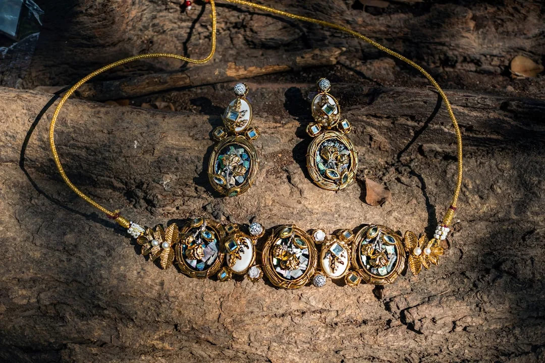 Eine goldene Halskette und passende Ohrringe mit verschlungenen Blumenmustern von GLAMESiA werden auf einer strukturierten Baumrindenoberfläche präsentiert.