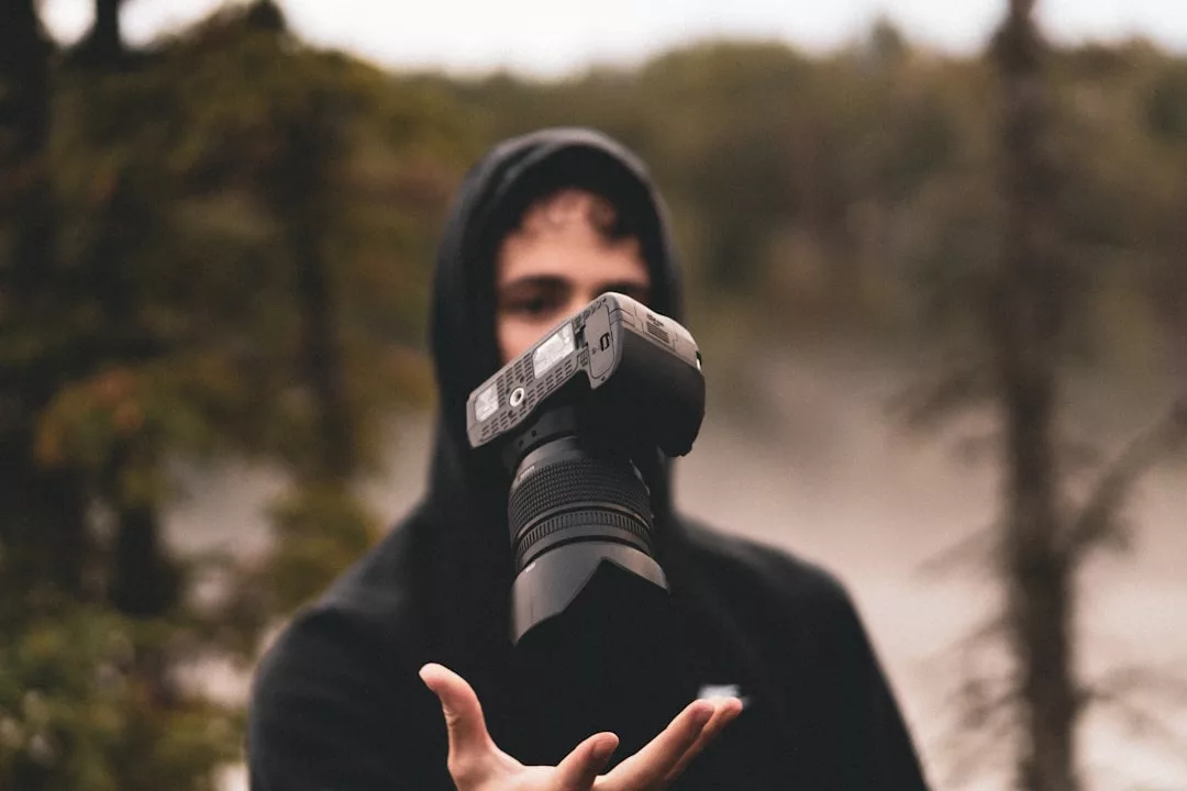 Eine Person in einem schwarzen Kapuzenpulli wirft eine GLAMESiA DSLR-Kamera im Freien in die Luft, wobei Bäume und ein unscharfer Hintergrund zu sehen sind.