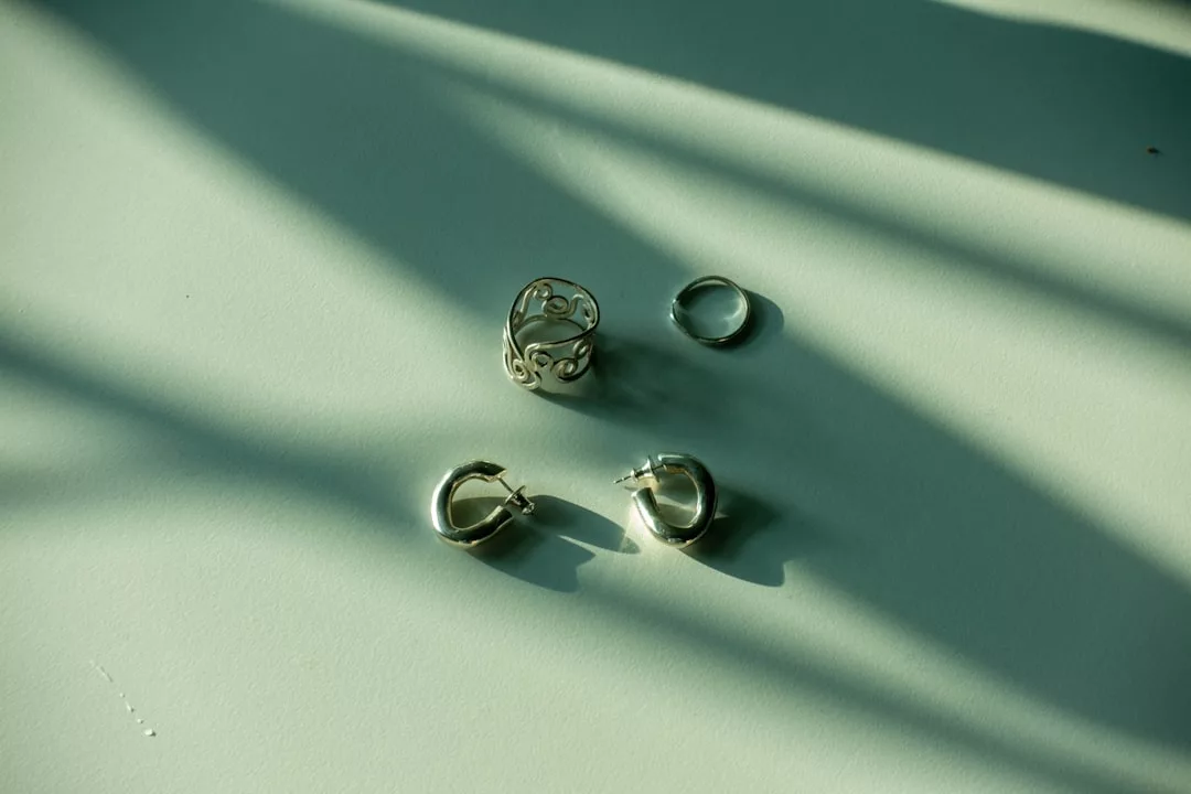 Vier silberne Ohrringe von GLAMESiA, darunter ein filigraner Ring und drei Reifmodelle, sind auf einer hellgrünen Fläche mit Schattenwurf angeordnet.