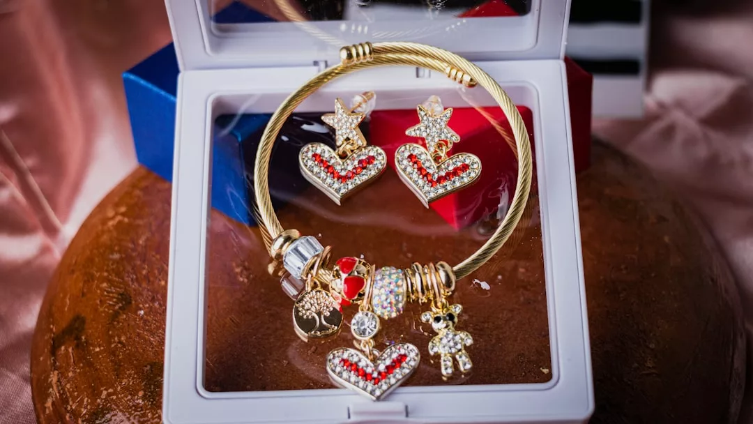 Ein goldenes Armband von GLAMESiA mit Anhängern in Herz- und Bärenform, gepaart mit passenden Ohrringen in Herzform, schön präsentiert in einer weißen Schmuckschatulle.