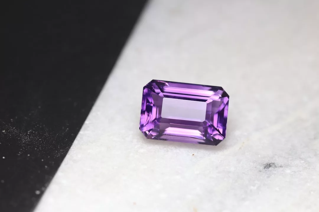 Ein violetter GLAMESiA-Edelstein im Rechteckschliff liegt auf einer weißen Marmorfläche mit einem schwarzen Streifen auf der linken Seite.