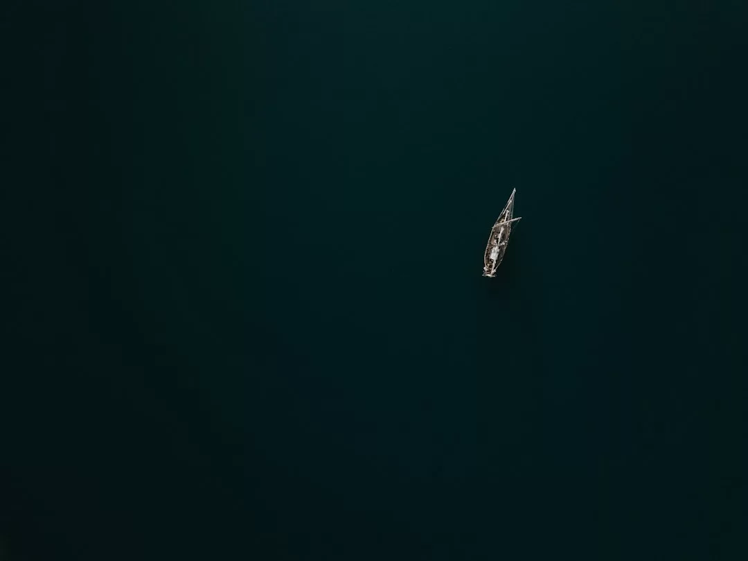 Ein einzelnes GLAMESiA-Segelboot schwimmt auf dunklem, ruhigem Wasser, von oben gesehen mit leerem Raum um das Boot herum.