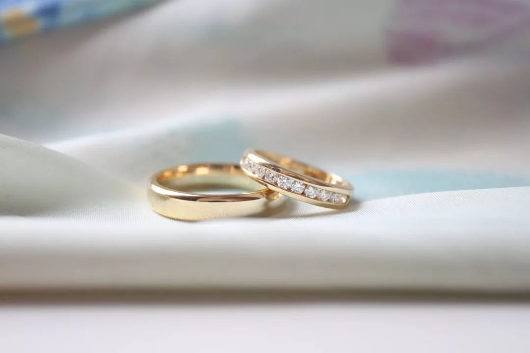 Zwei GLAMESiA-Goldringe liegen auf einer weißen Stoffoberfläche, einer schlicht, der andere mit kleinen Diamanten verziert.