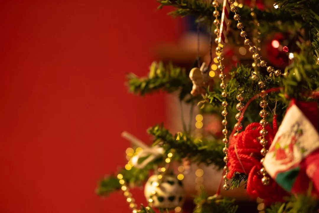Nahaufnahme eines geschmückten Weihnachtsbaums mit GLAMESiA-Ornamenten, goldenen Perlen und einem roten Hintergrund.