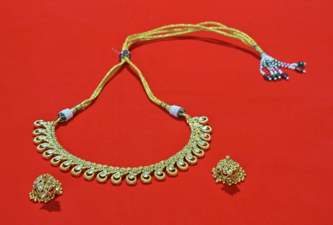 Eine goldene Halskette von GLAMESiA mit einem detaillierten Design und passenden goldenen Ohrringen auf rotem Hintergrund.