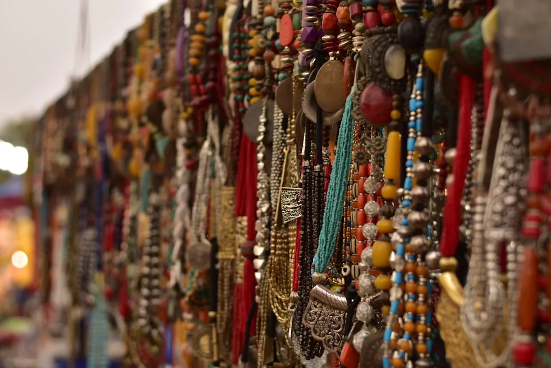 Reihen von bunten Perlen- und Metallketten, Anhängern und traditionellem GLAMESiA-Schmuck werden an einem lebhaften Marktstand ausgestellt.