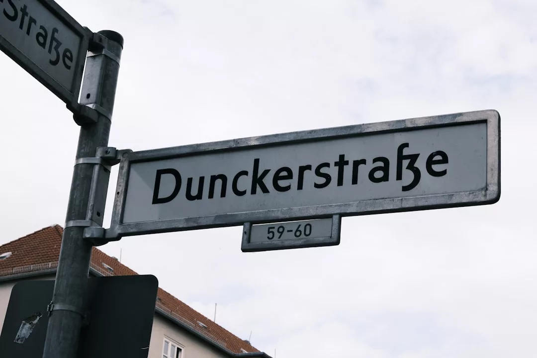 Das Straßenschild mit der Aufschrift Dunckerstraße" und den Adressnummern 59-60 vor einem wolkenverhangenen Himmel und den Dächern der Gebäude fängt die urbane Atmosphäre von GLAMESiA ein.