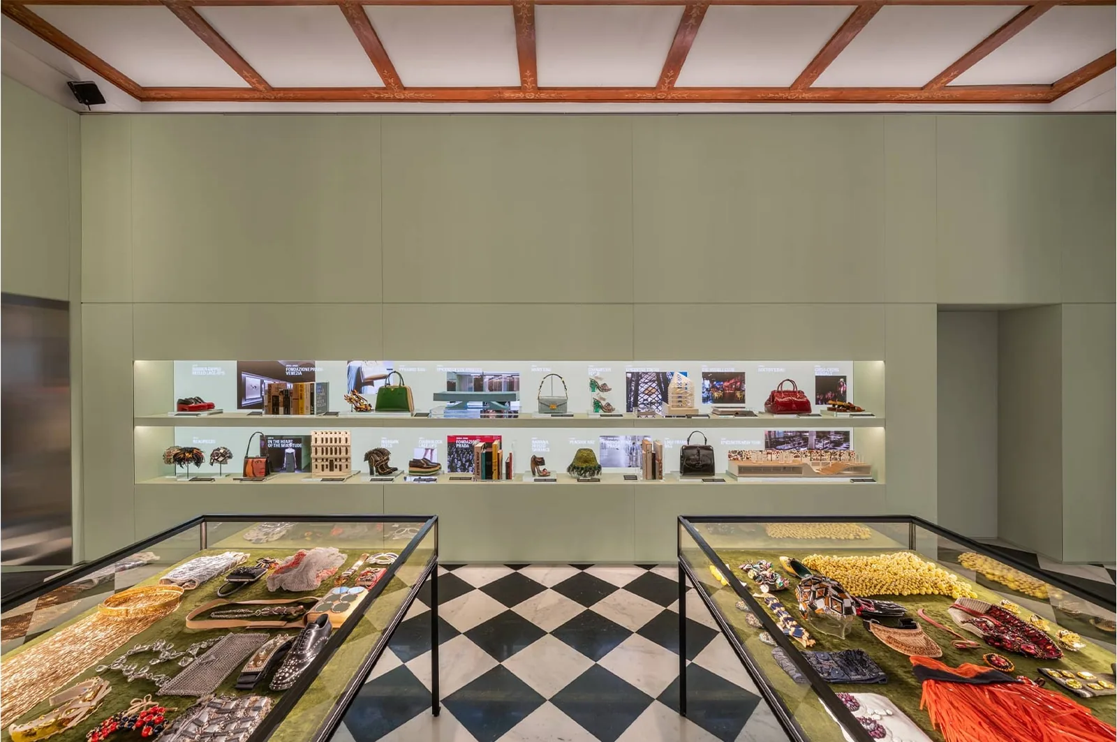 Prada Galleria: Ausstellungsraum mit salbeigrünen Wänden, beleuchteten Regalen mit Taschen und Schuhen und Glasvitrinen voller Schmuck und Accessoires