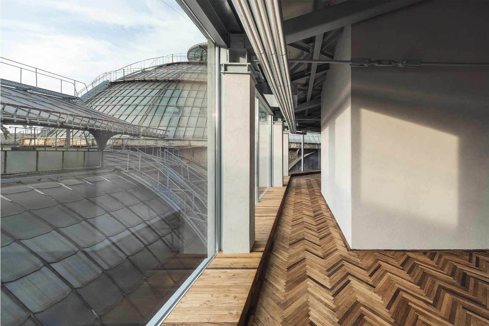 Prada Galleria: Gang mit Fischgrätparkett in einer oberen Etage, hinter der Glasfront das gewölbte Glasdach der Galleria