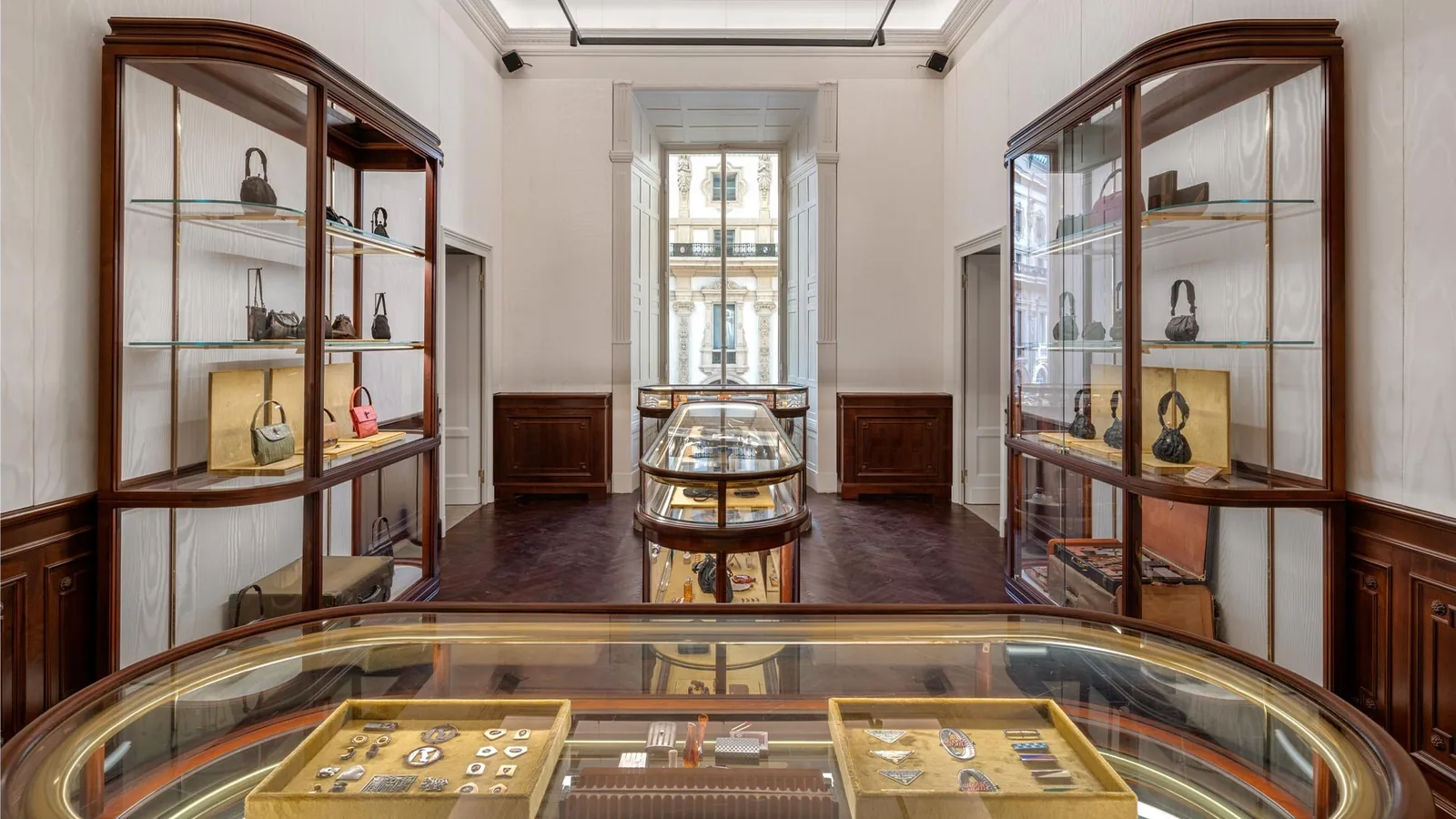Prada Galleria in Mailand: Raum mit hölzernen Vitrinen voller Taschen und einer ovalen Glasvitrine mit Archivstücken