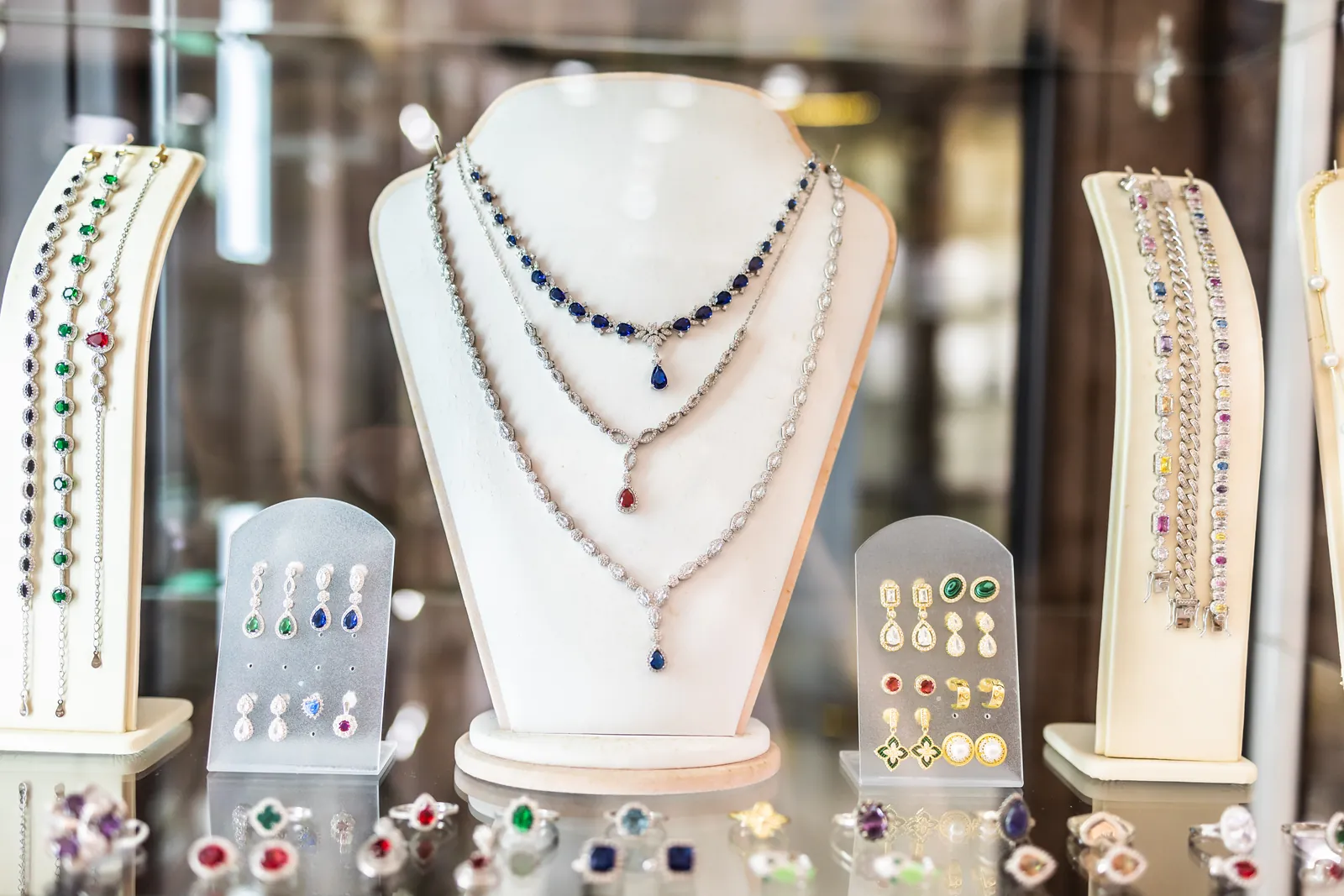 Vitrine eines Juweliers mit Colliers, Armbändern, Ohrsteckern und Ringen, besetzt mit blauen, roten und grünen Edelsteinen.