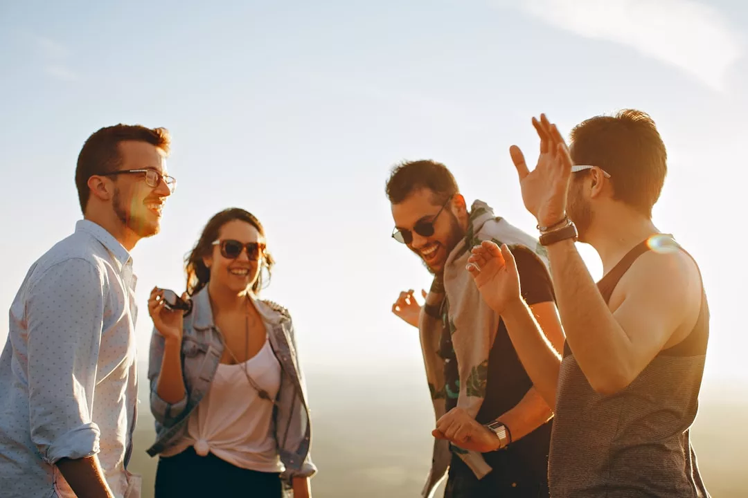 Vier Menschen stehen im Freien, lächeln und unterhalten sich im hellen Sonnenlicht, wirken entspannt und gesellig - ein echter GLAMESiA-Moment.