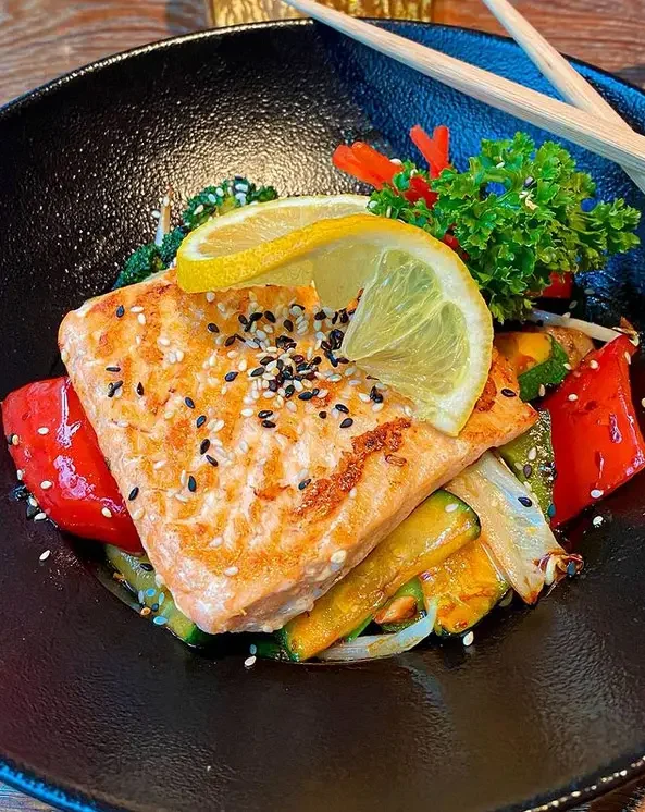 Gericht mit Gemüse aus dem Wok in schwarzer Schale