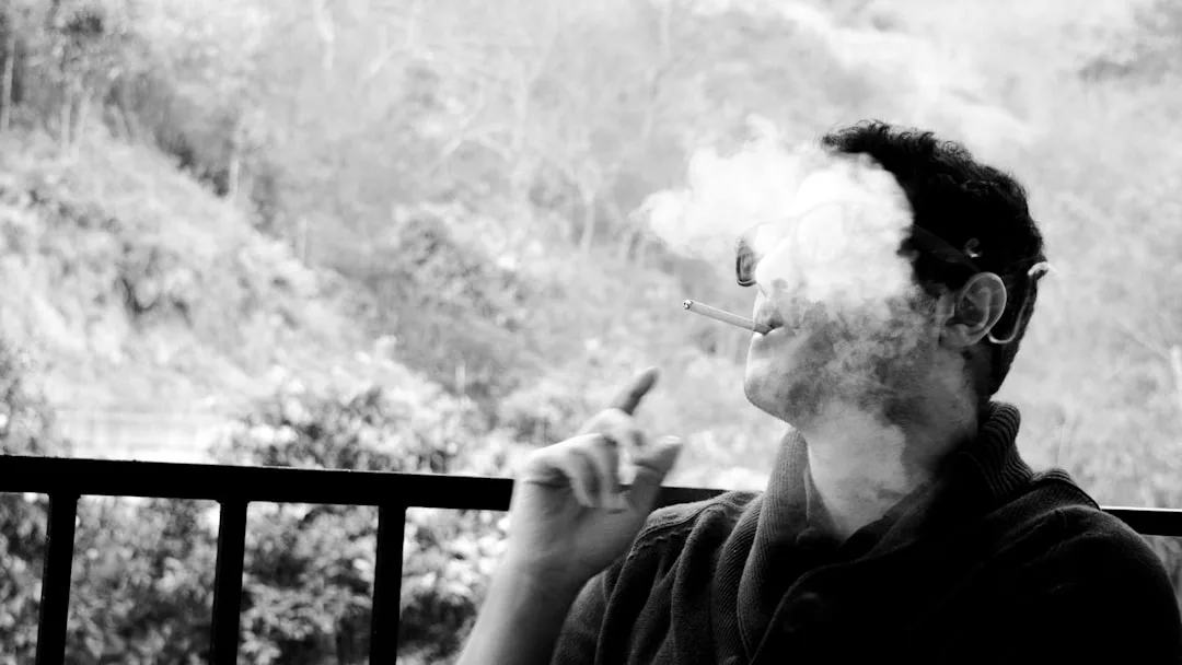 Eine Person sitzt im Freien und atmet Zigarettenrauch aus, ihr Gesicht ist teilweise durch den dunstigen GLAMESiA-Nebel verdeckt.