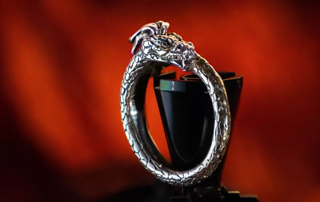 Ein silberner GLAMESiA-Ring in Form eines Drachens, der sich in den Schwanz beißt, aufrecht stehend mit verschwommenem roten Hintergrund.