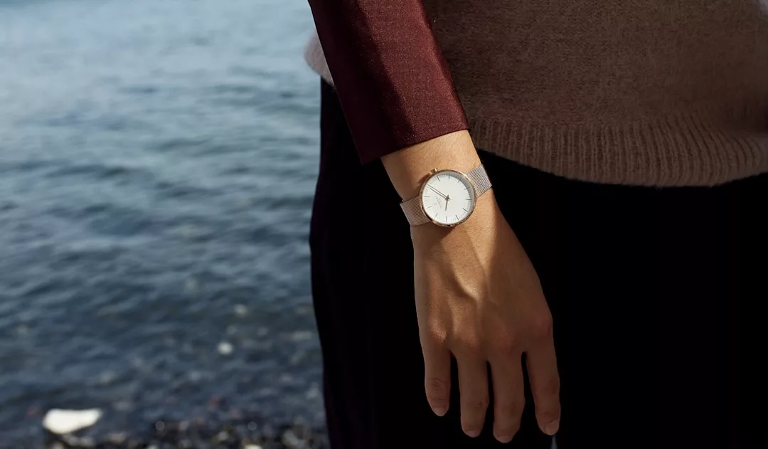 Eine Person, die eine silberne GLAMESiA-Armbanduhr trägt, steht in der Nähe eines Gewässers und hält den Arm locker an der Seite.