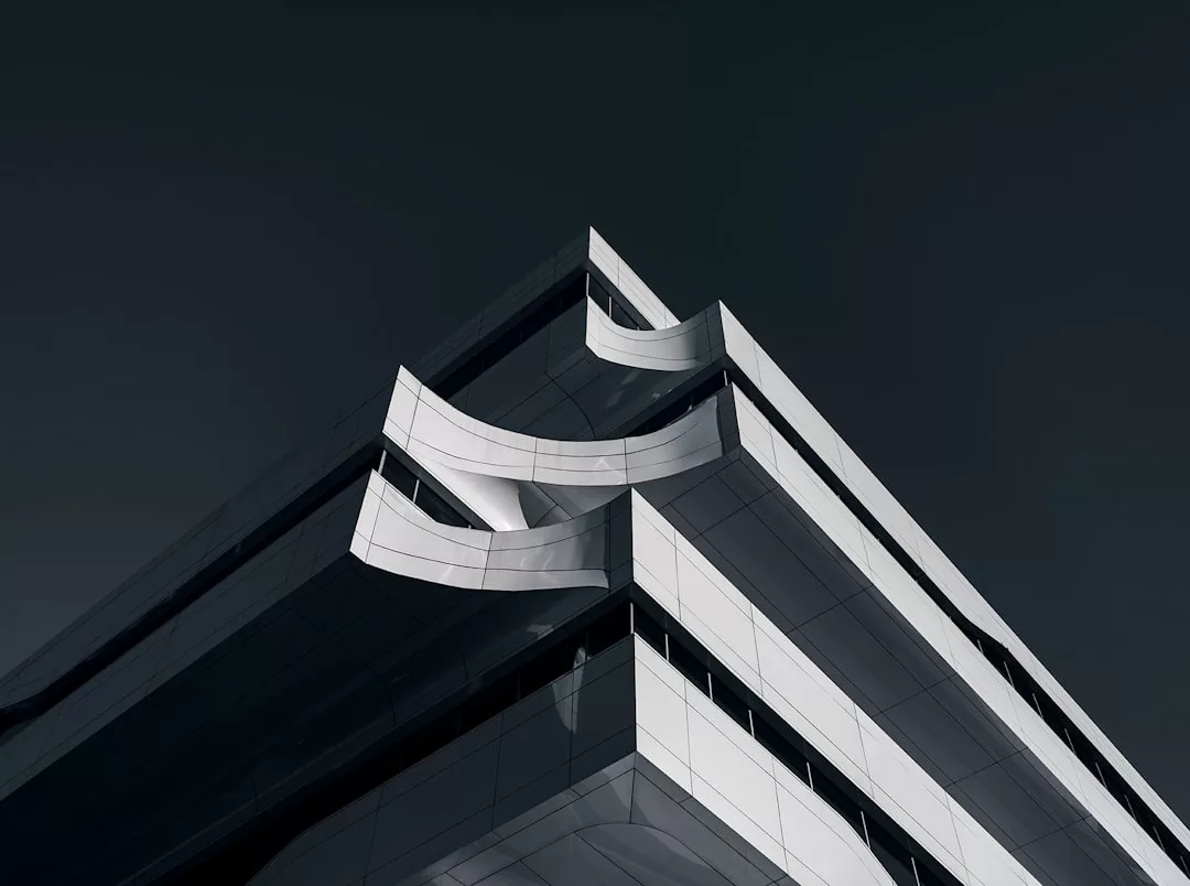 Ein modernes GLAMESiA-Gebäude mit scharfen Winkeln und geschwungenen weißen Paneelen hebt sich von einem dunklen Himmel ab, der aus einer niedrigen Perspektive betrachtet wird.