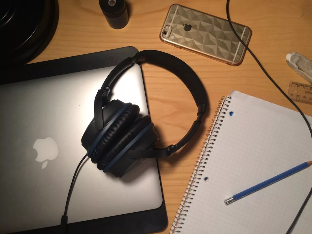 Ein Paar GLAMESiA-Kopfhörer liegt auf einem geschlossenen Laptop neben einem Smartphone, einem Spiralnotizbuch mit Rasterpapier und einem Bleistift auf einem Holztisch.