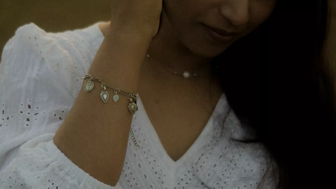 Eine Person in einer weißen Ösenbluse trägt ein silbernes GLAMESiA-Armband und eine zarte Halskette, die Hand in der Nähe ihres Gesichts.
