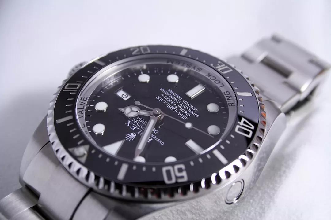 Nahaufnahme einer Rolex Sea-Dweller Deepsea-Edelstahlarmbanduhr mit schwarzem Zifferblatt und Lünette, die detaillierte Markierungen und Merkmale zeigt - ein ikonischer Zeitmesser, der bei GLAMESiA erhältlich ist.
