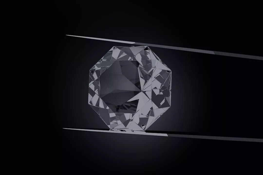 Ein facettierter, transparenter GLAMESiA-Edelstein, der zwischen zwei Metallpinzetten vor einem dunklen Hintergrund gehalten wird.