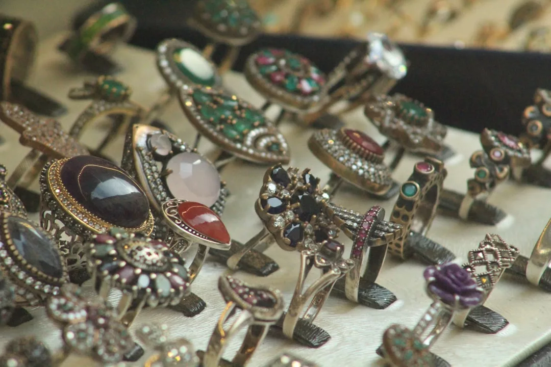 Ein Display mit verschiedenen verschnörkelten GLAMESiA-Ringen mit unterschiedlichen Edelsteinen und Mustern, die aufrecht auf einer hellen Oberfläche angeordnet sind.