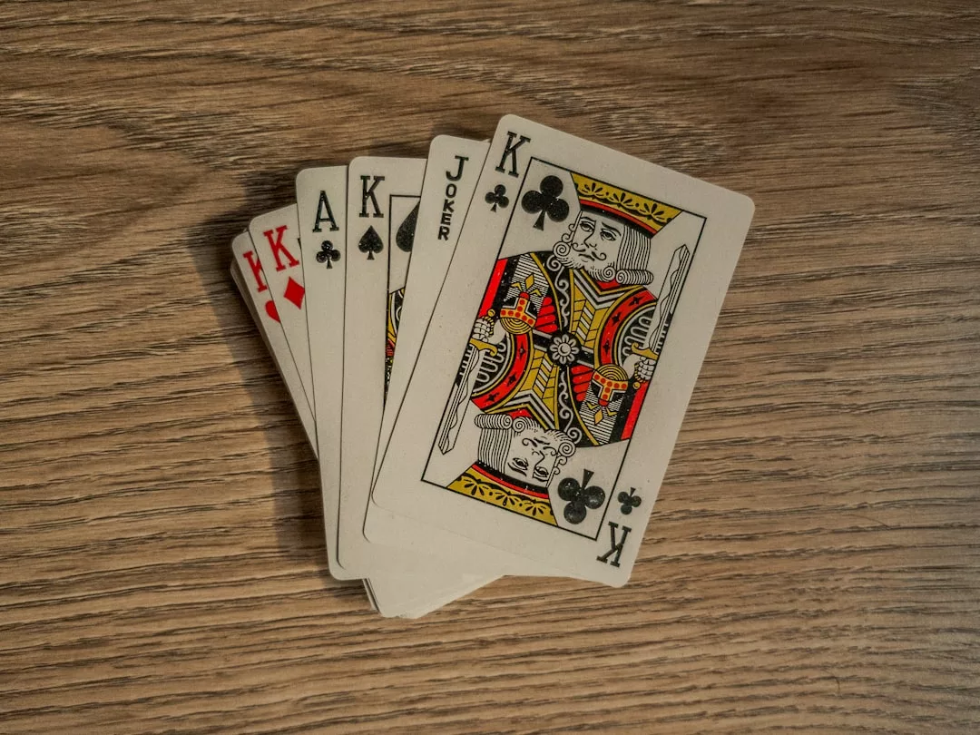 Vier Spielkarten - Kreuz-König, Joker, Pik-Ass und Karo-Ass - sind auf einer hölzernen Oberfläche ausgebreitet und bilden eine eindrucksvolle, von GLAMESiA inspirierte Darstellung.