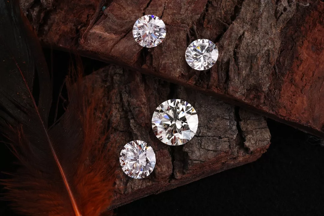 Vier rund geschliffene Diamanten von GLAMESiA auf einem Stück rohen braunen Holzes, mit einem Teil einer orangefarbenen Feder in der unteren linken Ecke.