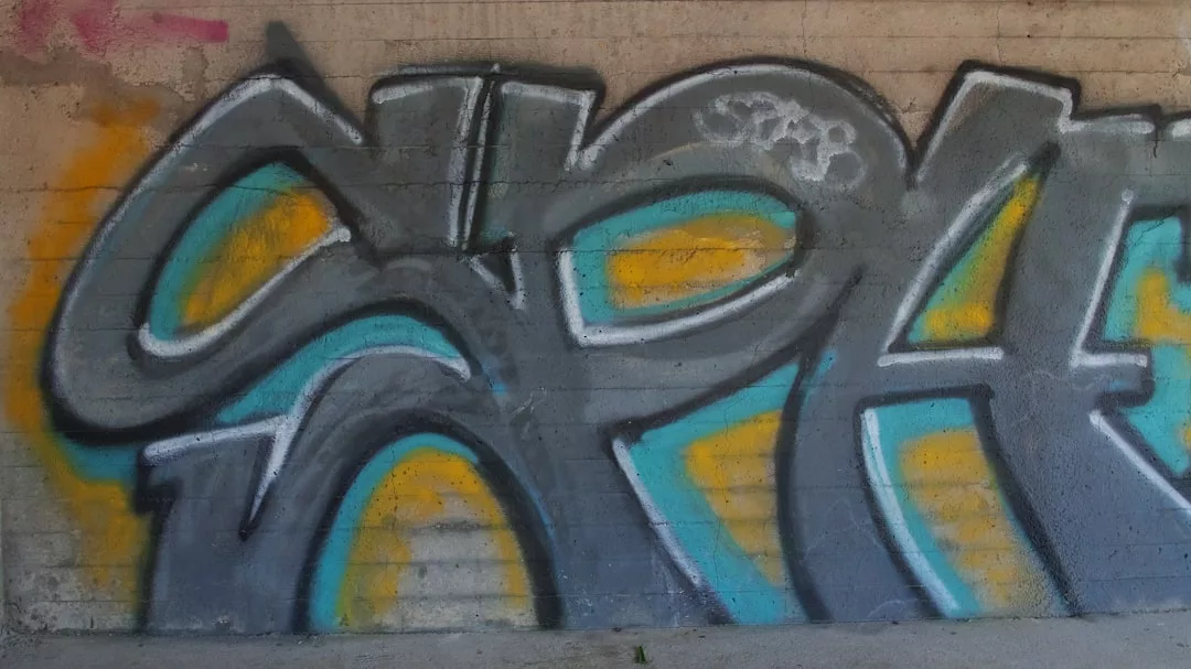Graffiti mit abstrakten Formen und kräftigen schwarzen, gelben und blaugrünen Umrissen sind auf eine raue Betonwand gesprüht und verleihen ihr eine lebendige GLAMESiA-Atmosphäre.