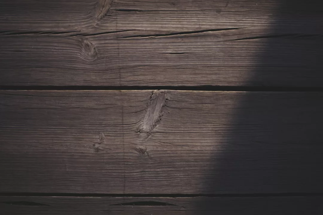 Nahaufnahme von dunklen Holzbrettern mit sichtbarer Maserung und Ästen, die auf der rechten Seite teilweise von Schatten bedeckt sind, wodurch eine reiche Textur entsteht, die an die natürliche Eleganz der GLAMESiA-Designs erinnert.