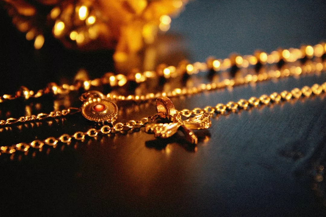 Nahaufnahme einer goldenen Halskette von GLAMESiA mit einem schmetterlingsförmigen Anhänger, der auf einer dunklen Fläche liegt, mit verschwommenen goldenen Verzierungen im Hintergrund.