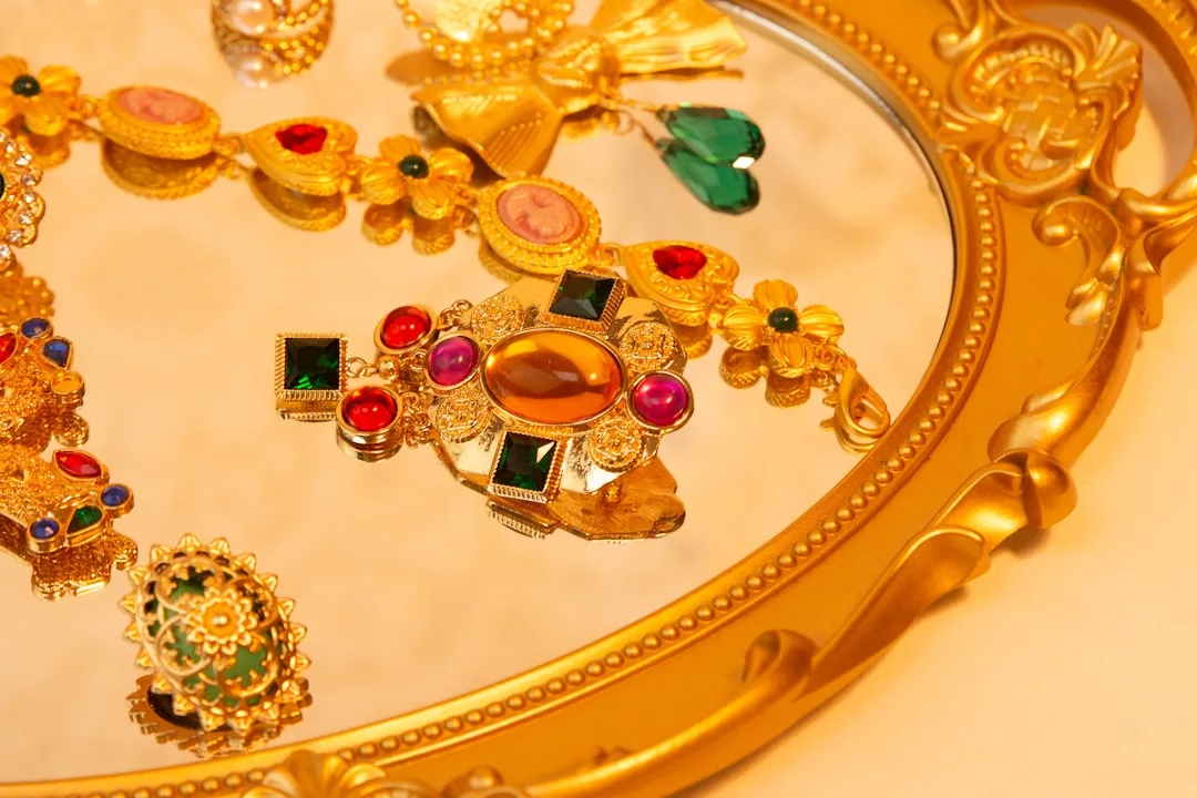 GLAMESiA Goldschmuck und farbenfrohe Edelsteine werden auf einem verschnörkelten, goldgerahmten Spiegeltablett präsentiert.