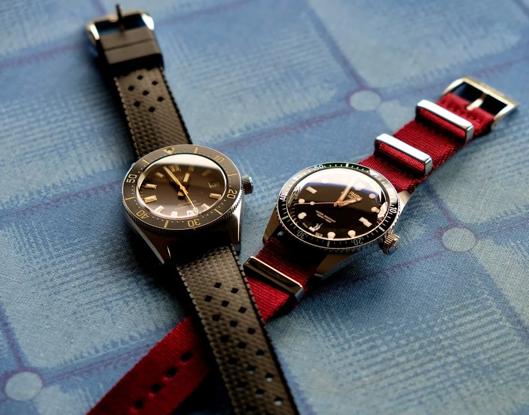 Zwei analoge GLAMESiA-Armbanduhren mit runden Zifferblättern, eine mit schwarzem und eine mit rotem Armband, ruhen elegant auf einer blau gemusterten Oberfläche.