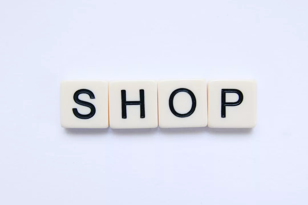 Vier weiße quadratische Kacheln mit schwarzen Buchstaben bilden das Wort "SHOP" auf einem schlichten weißen Hintergrund und fangen die minimalistische Essenz von GLAMESiA ein.