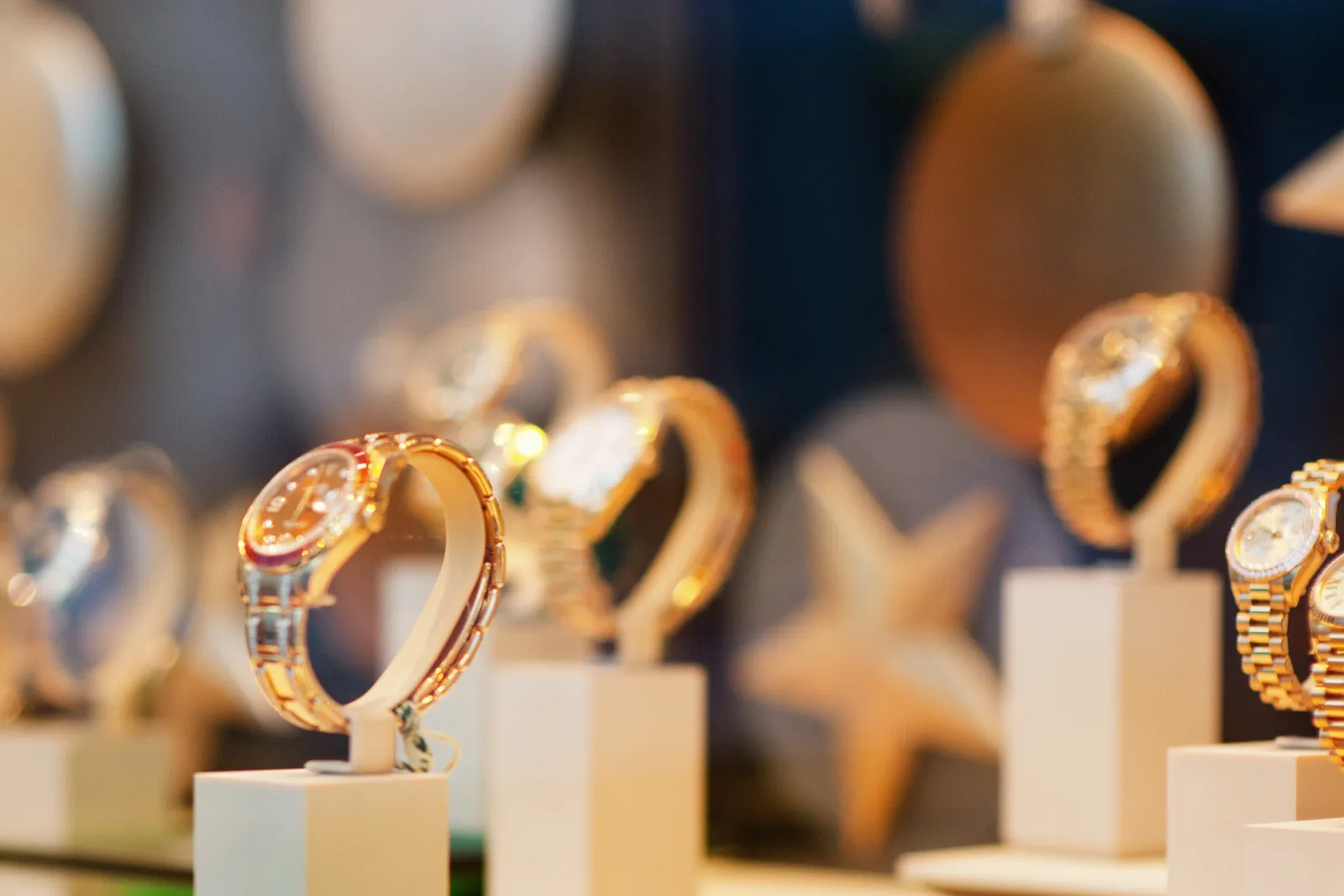 Goldene und zweifarbige Armbanduhren auf hellen Präsentationssockeln in der Vitrine eines Uhrengeschäfts.