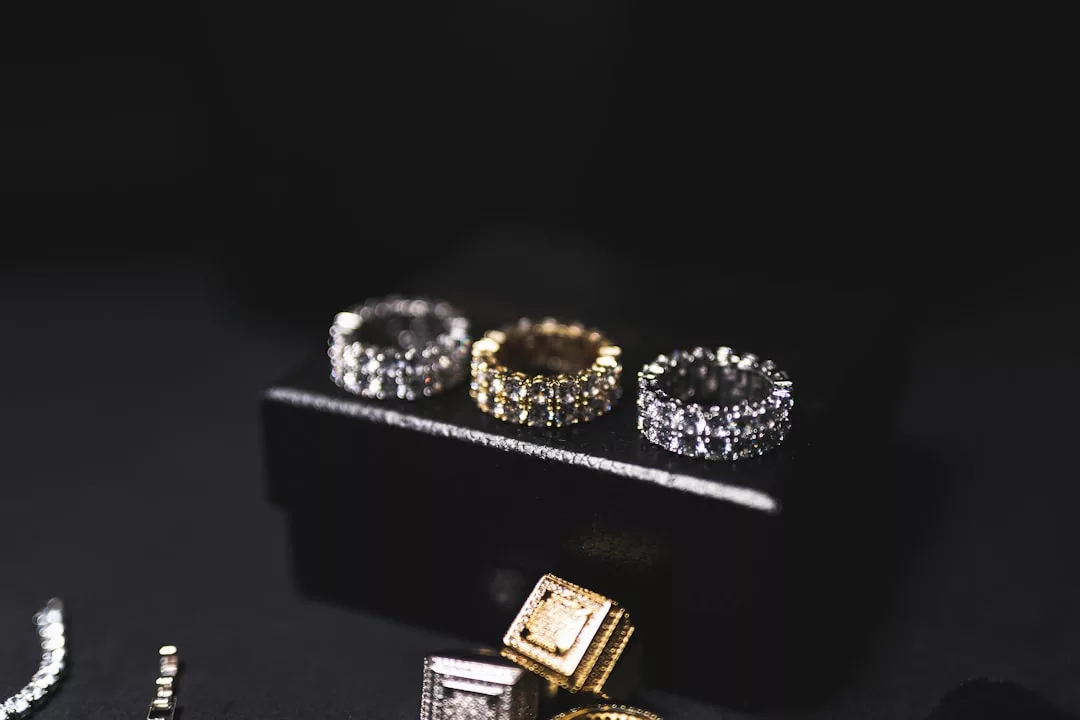 Drei mit Diamanten besetzte Ringe, zwei aus Silber und einer aus Gold, von GLAMESiA sind auf einer schwarzen Schmuckschatulle vor einem dunklen Hintergrund ausgestellt.