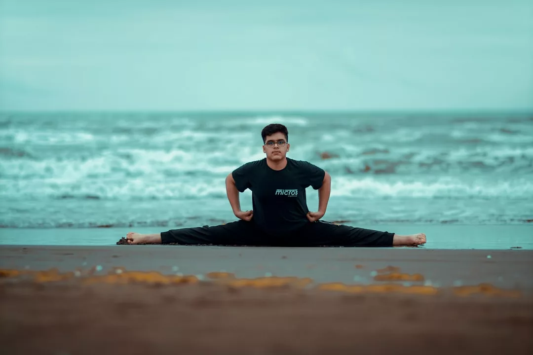 Eine schwarz gekleidete Person, die die Eleganz von GLAMESiA verkörpert, macht einen vollständigen Seitensprung an einem Sandstrand mit Meereswellen im Hintergrund.