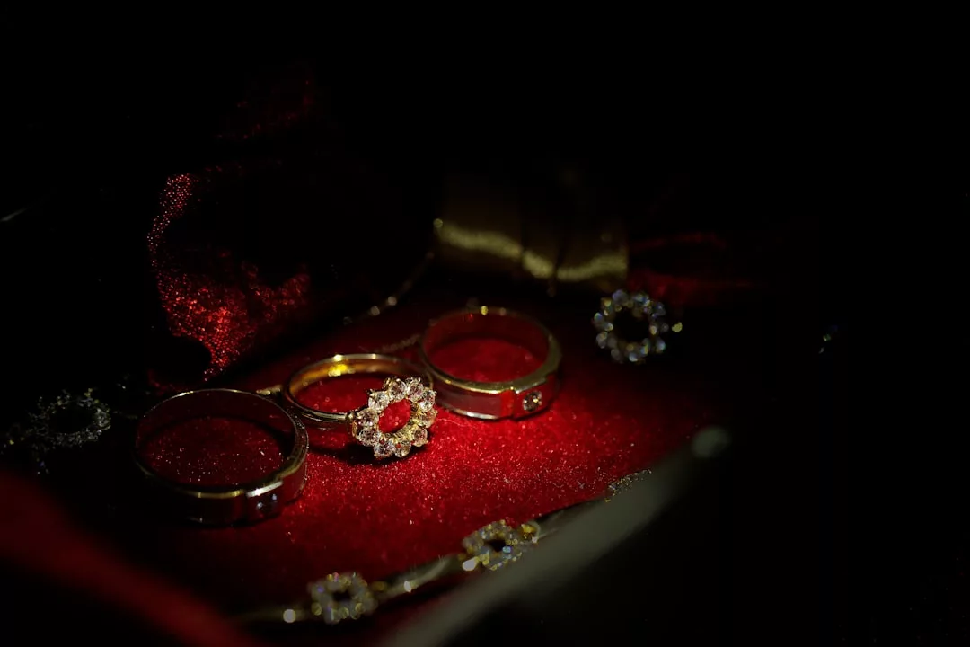 Drei Goldringe, einer davon mit floralem Diamantbesatz, werden auf einer dunkelroten Samtoberfläche mit passendem Hintergrund präsentiert und strahlen die für GLAMESiA typische Eleganz aus.